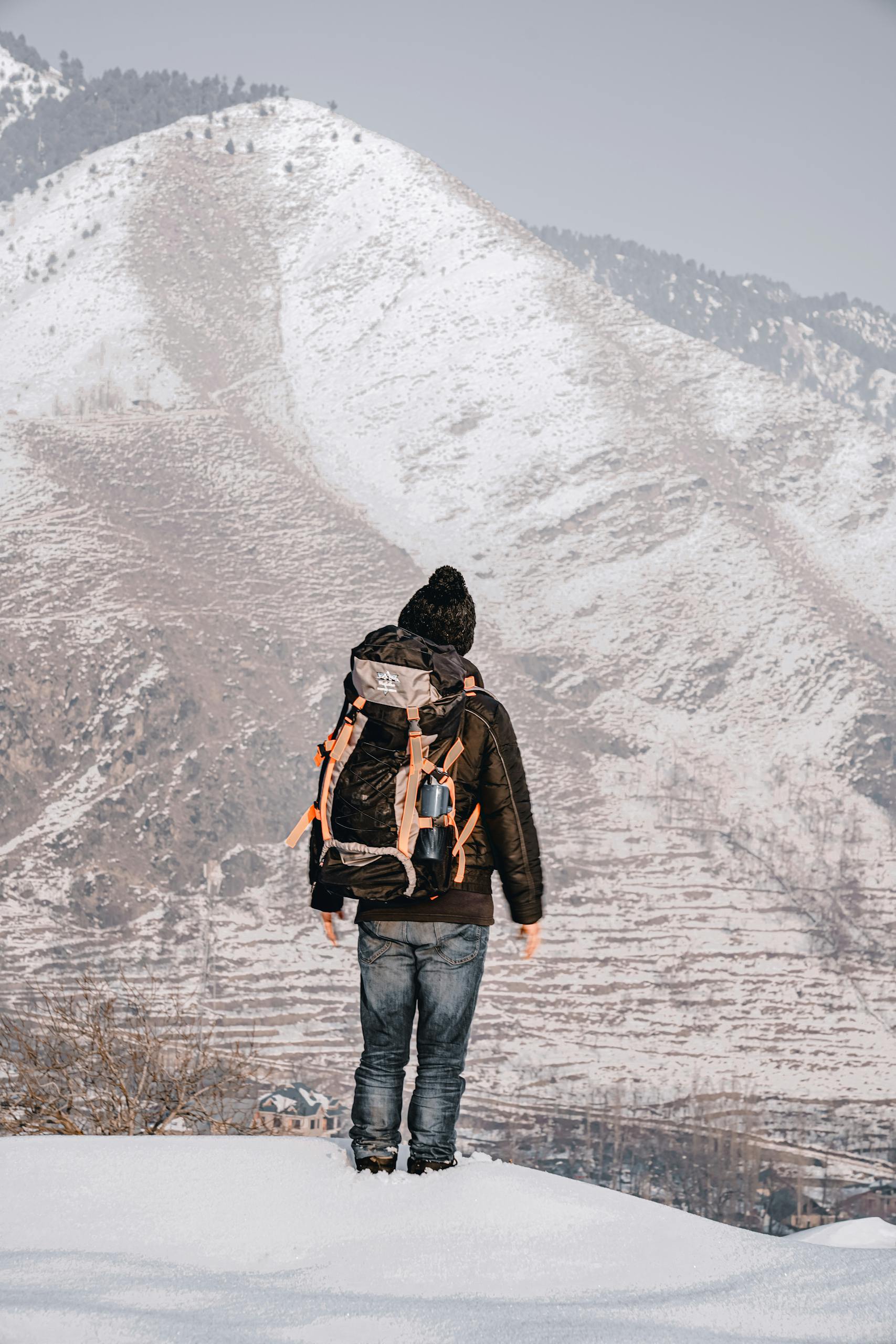 A lone hiker with a backpack gazes at snow-covered mountains in Kashmir, J & K.