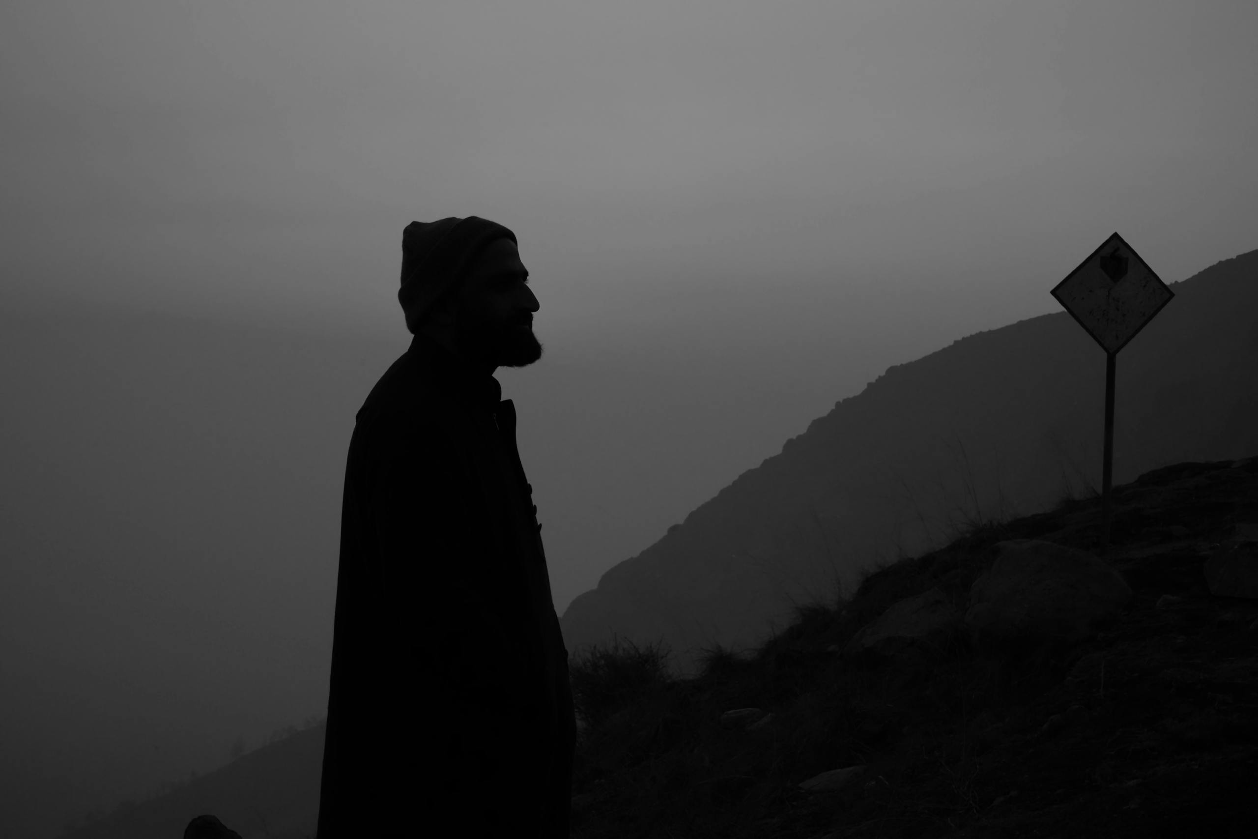 Silhouetted man in beanie against misty Srinagar hills, serene and contemplative at dawn.